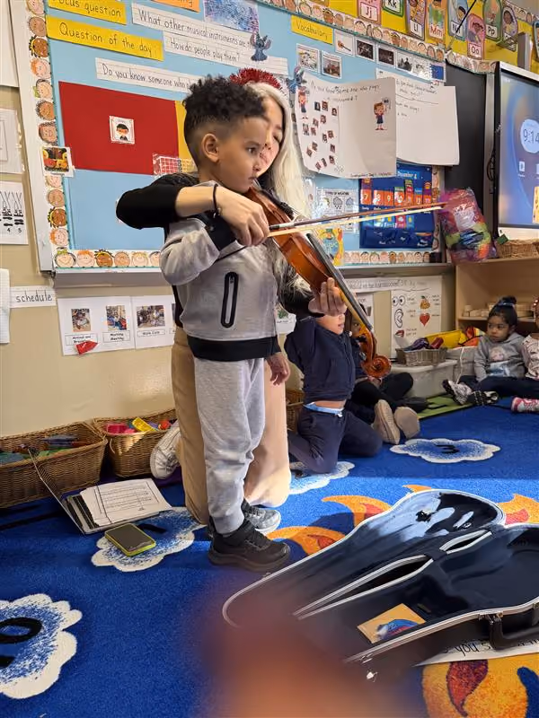 Student tries playing violin with teacher's guidance in classroom