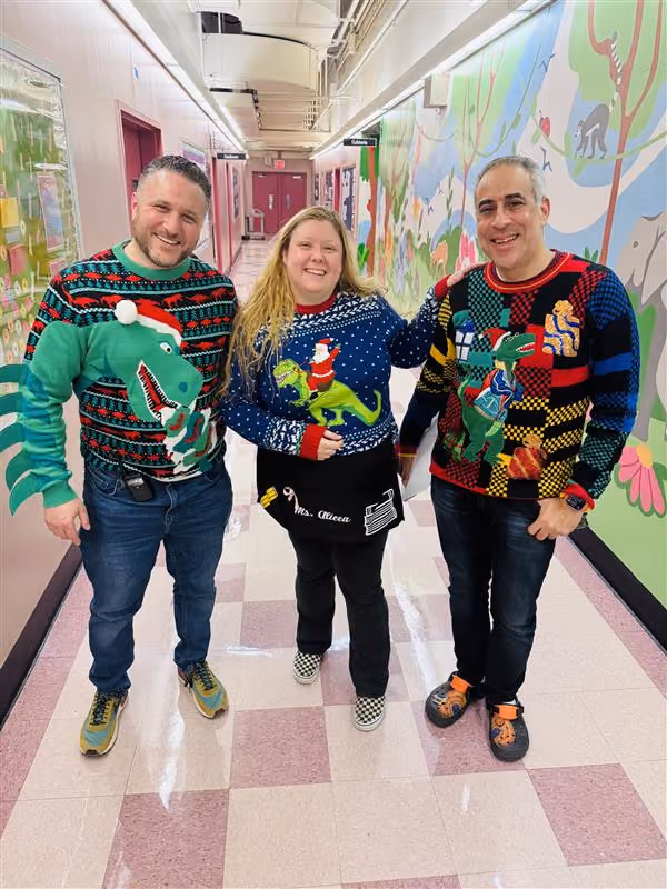 Three staff members wearing holiday ugly sweaters in school hallway