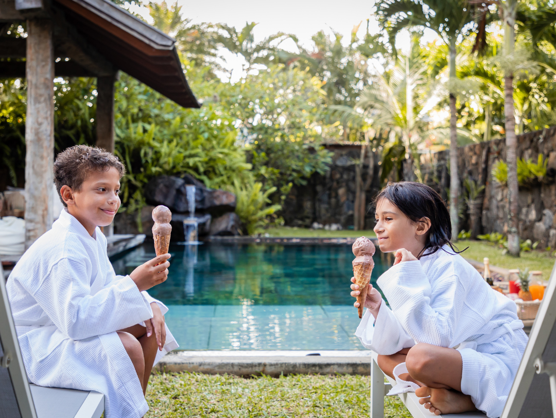 Two Kids Enjoying an Ice Cream in Front of A Private Pool