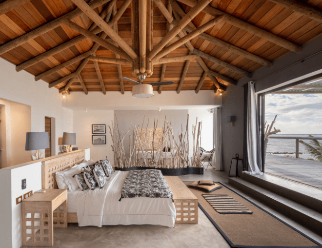 Spacious bedroom with wooden ceiling, large bed, and ocean view terrace