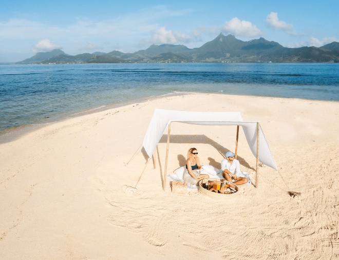 Romantic setup on a tropical beach with shade tent, food, and ocean view