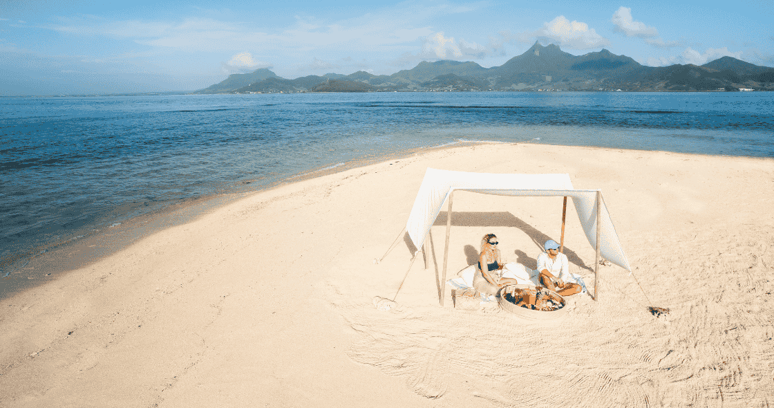 Couple enjoying a beach picnic under a canopy on a secluded sandy shore