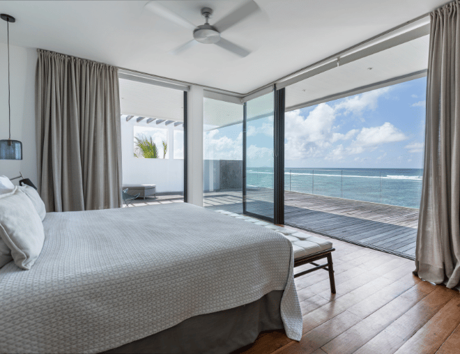 Bright white bedroom featuring a wooden deck and ocean horizon.