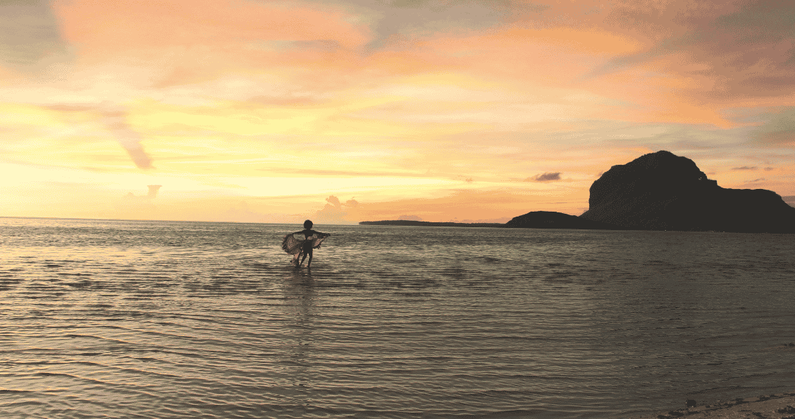 Silhouette of a person standing in the ocean at sunset.