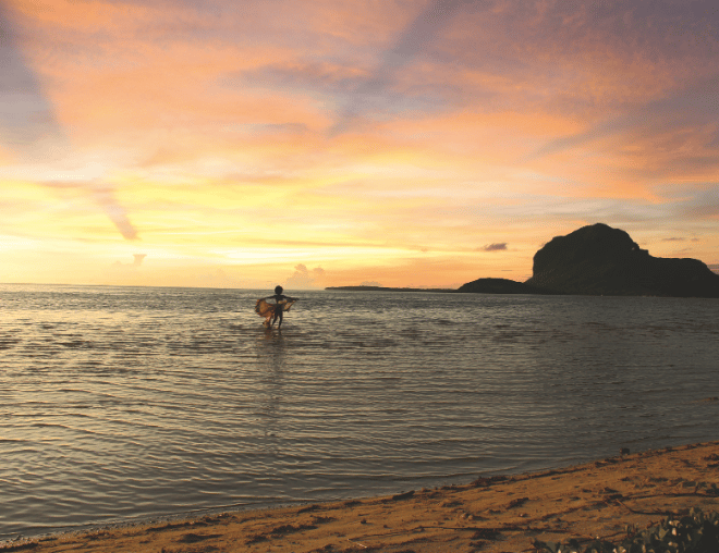 Person silhouetted in calm shallow water during a golden sunset.