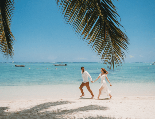 A couple enjoying a romantic run by the ocean on a sunny day, wearing breezy summer clothes.