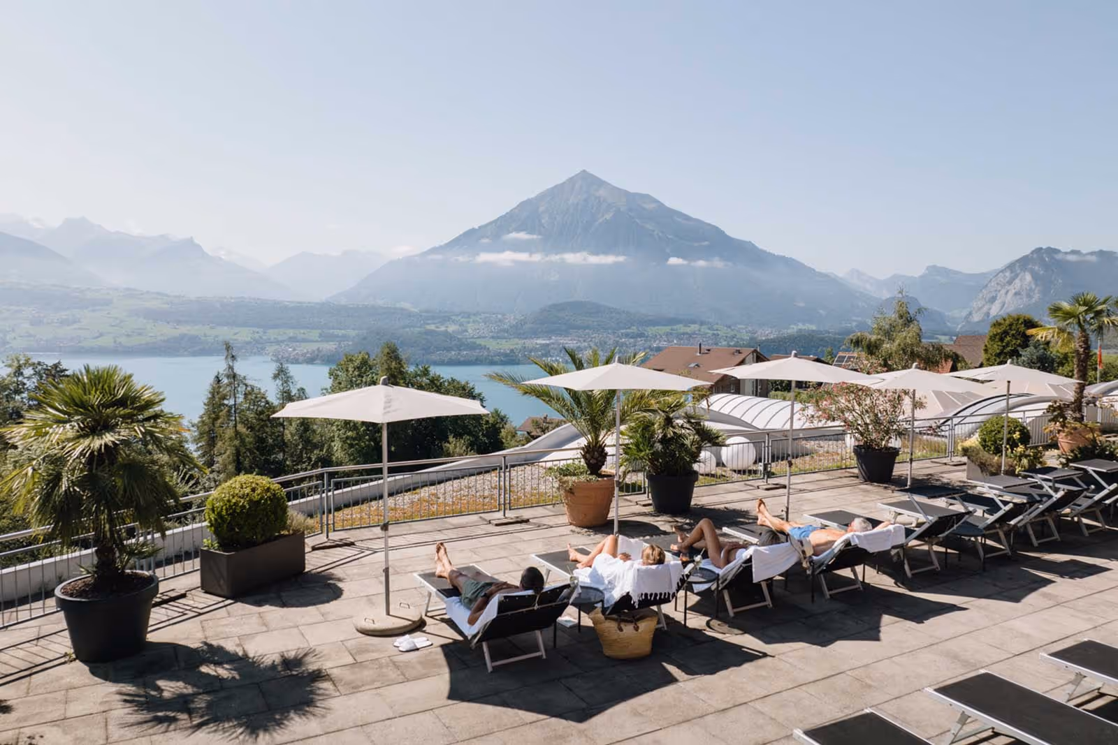 Grande terrasse avec chaises longues et parasols avec vue sur le lac de Thoune et le Niesen.