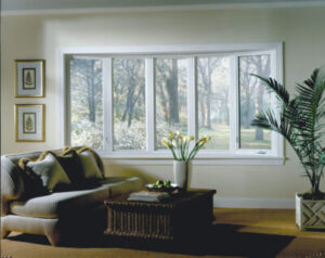 A cozy-looking room featuring a bay window that overlooks a wooded area