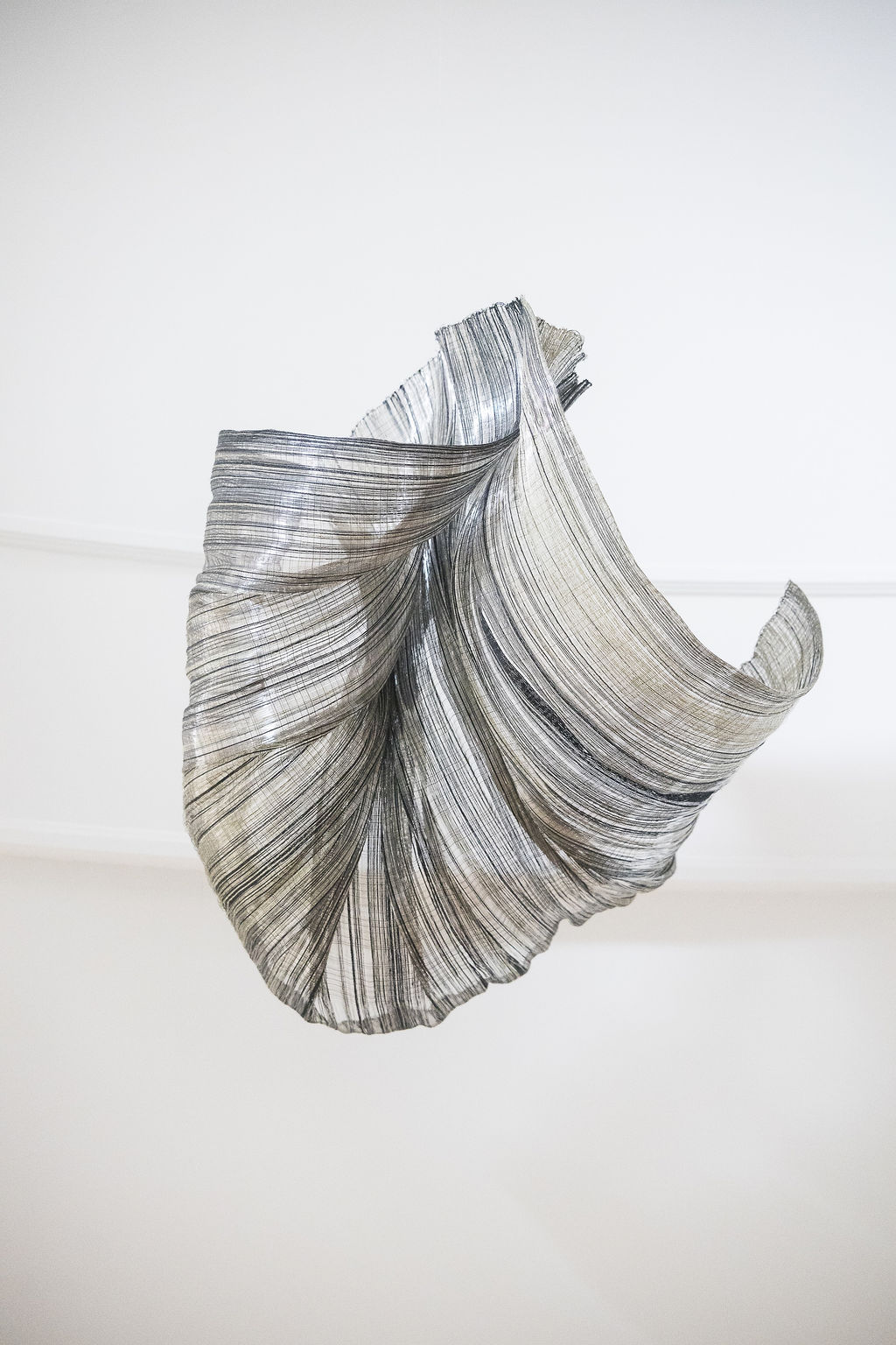 Adeline Halot transforms raw materials into poetic, architectural works of art. With a background in interior architecture and textile design from La Cambre, she merges spatial thinking with a tactile understanding of fiber. Her practice is a bold exploration of texture, form, and light—sculpting woven compositions from metallic wire and flax linen yarn. Each piece is a striking balance of nature and technology. Inspired by organic and mineral formations, Adeline's sculptures come alive through dynamic shapes and layered surfaces that shift with light and shadow. More than decorative objects, they are immersive experiences—fluid in meaning, adaptable in space, and rooted in a deep material curiosity. Adeline Halot’s work invites the viewer to slow down and engage with the subtleties of structure and surface. These are not just artworks; they are living spaces within themselves.