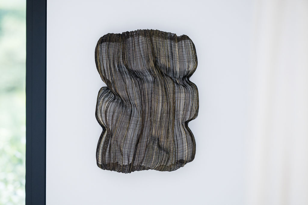 Adeline Halot transforms raw materials into poetic, architectural works of art. With a background in interior architecture and textile design from La Cambre, she merges spatial thinking with a tactile understanding of fiber. Her practice is a bold exploration of texture, form, and light—sculpting woven compositions from metallic wire and flax linen yarn. Each piece is a striking balance of nature and technology. Inspired by organic and mineral formations, Adeline's sculptures come alive through dynamic shapes and layered surfaces that shift with light and shadow. More than decorative objects, they are immersive experiences—fluid in meaning, adaptable in space, and rooted in a deep material curiosity. Adeline Halot’s work invites the viewer to slow down and engage with the subtleties of structure and surface. These are not just artworks; they are living spaces within themselves.