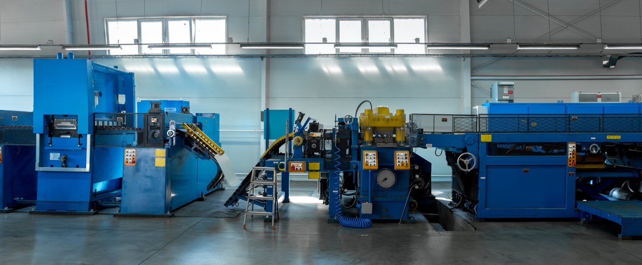 Große blaue industrielle Maschine in einer hellen Fabrikumgebung mit einem Förderband und Steuerpaneelen.