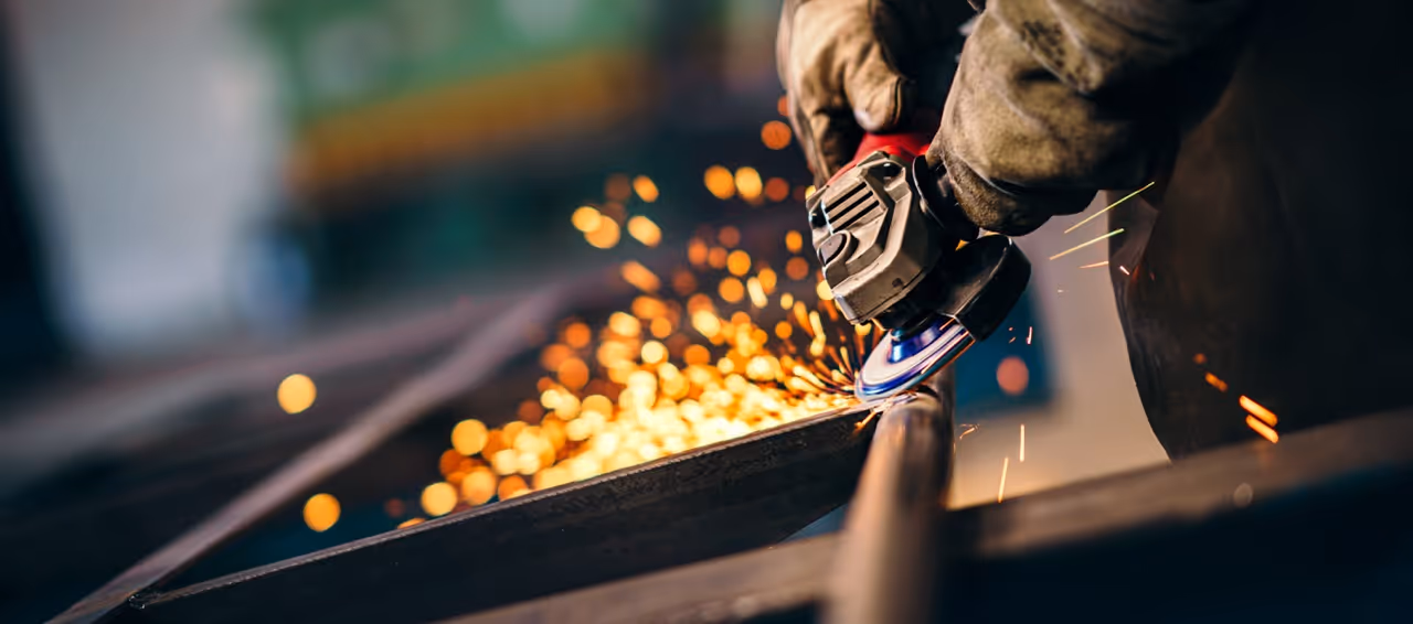 Person schneidet Metall mit Winkelschleifer, Funken fliegen.