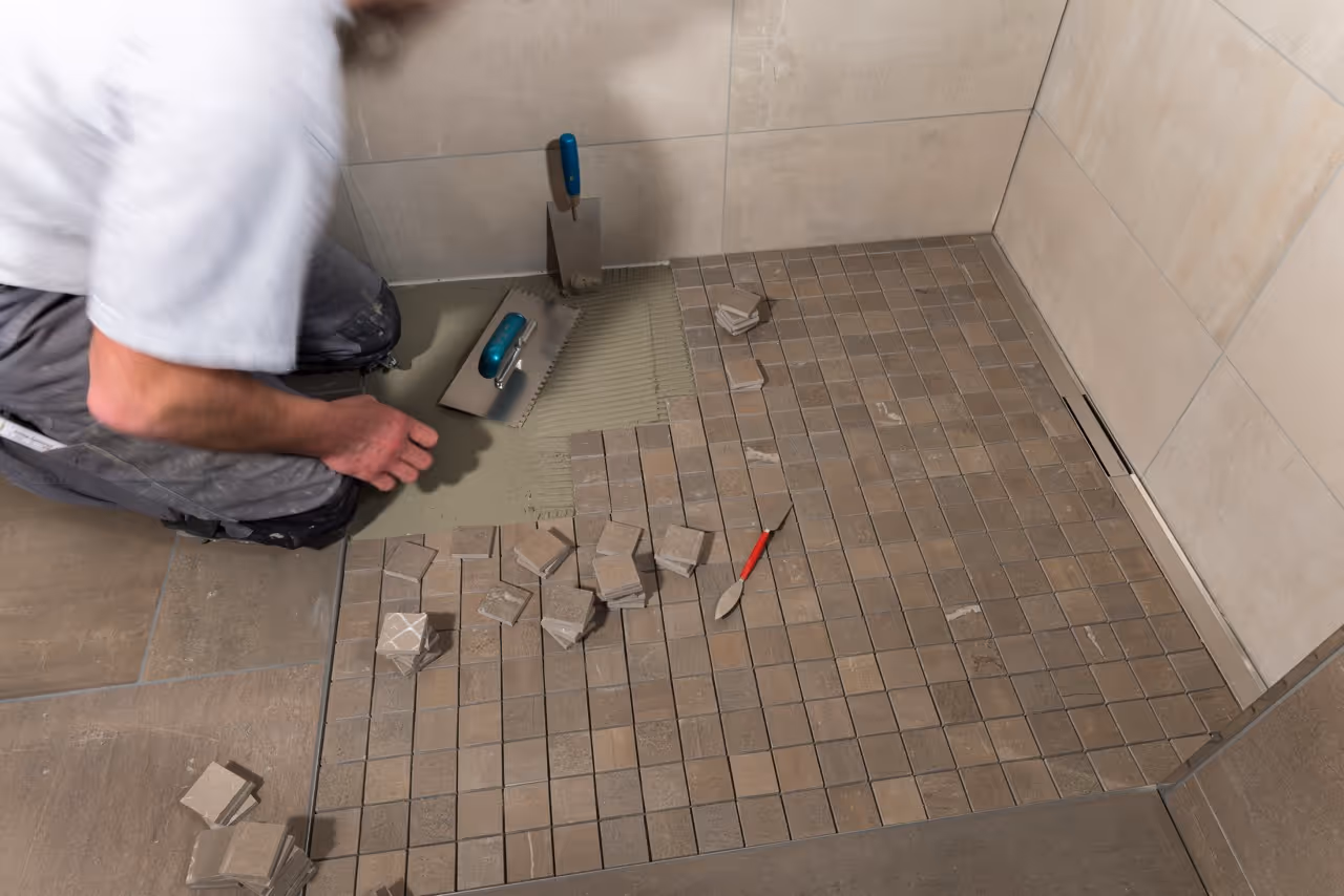 Handwerker verlegt kleine quadratische Bodenkacheln auf den Boden eines Badezimmers.