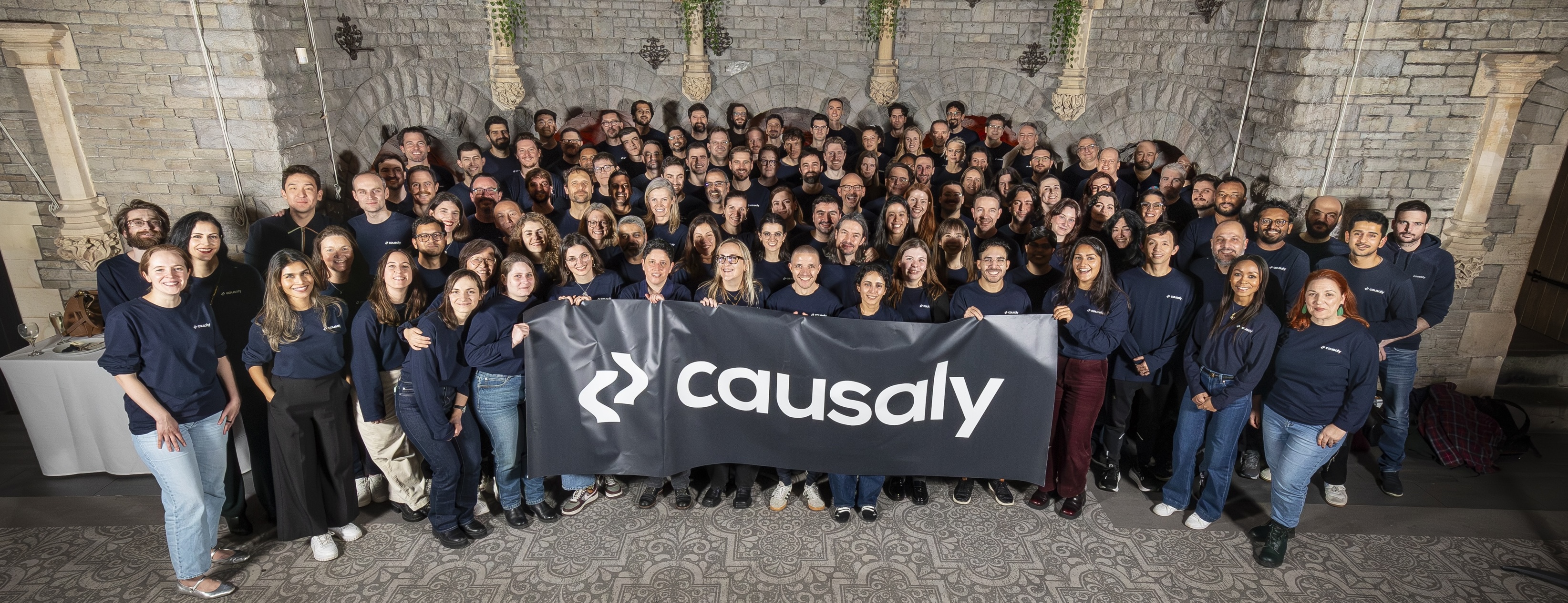 A happy Causaly team holding a large logo banner