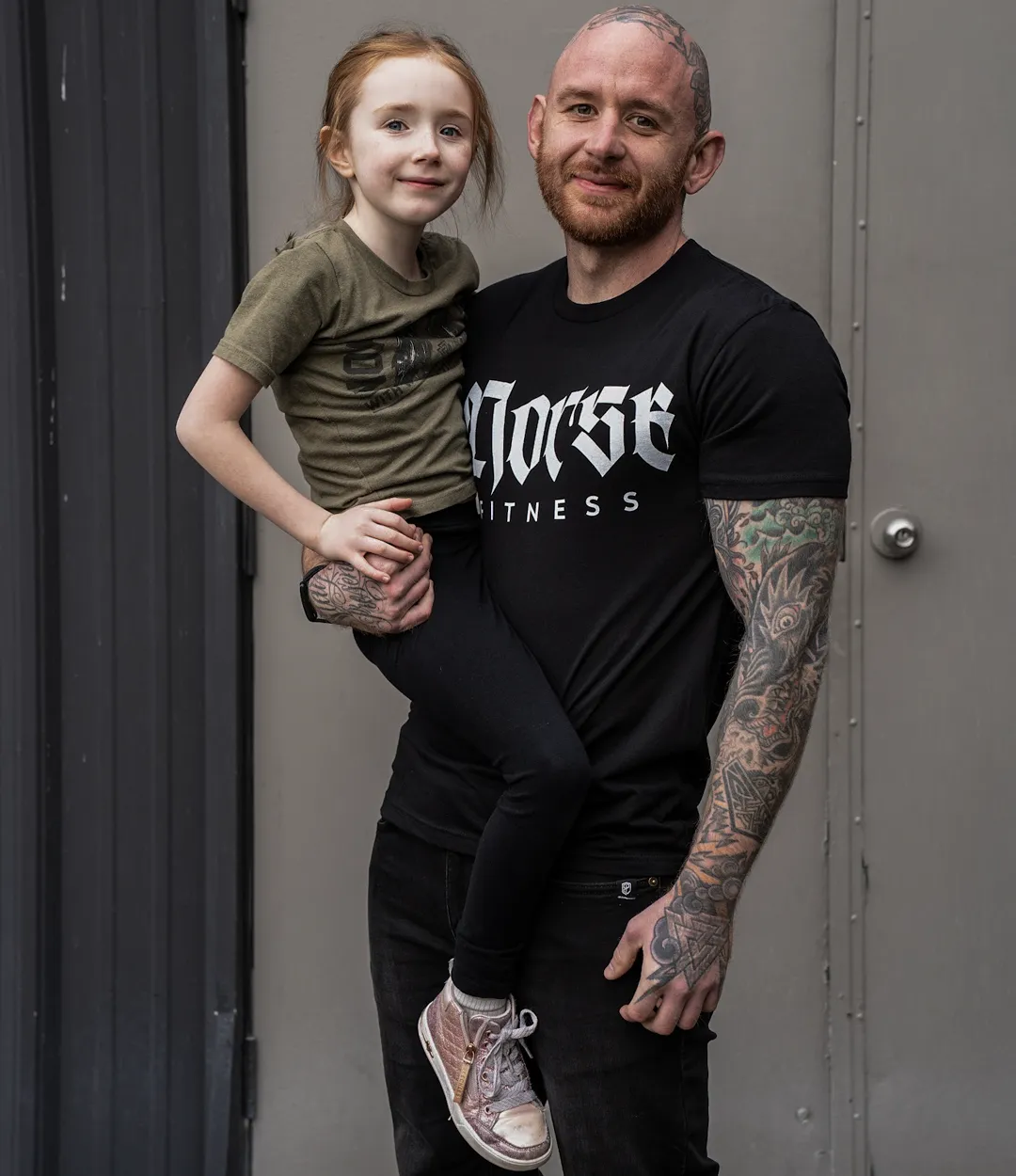 Andrew Lewis holding his daughter, both smiling, wearing a Norse Fitness shirt