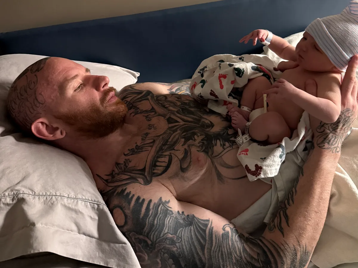 Andrew Lewis lying in a hospital bed with his newborn son resting on his chest