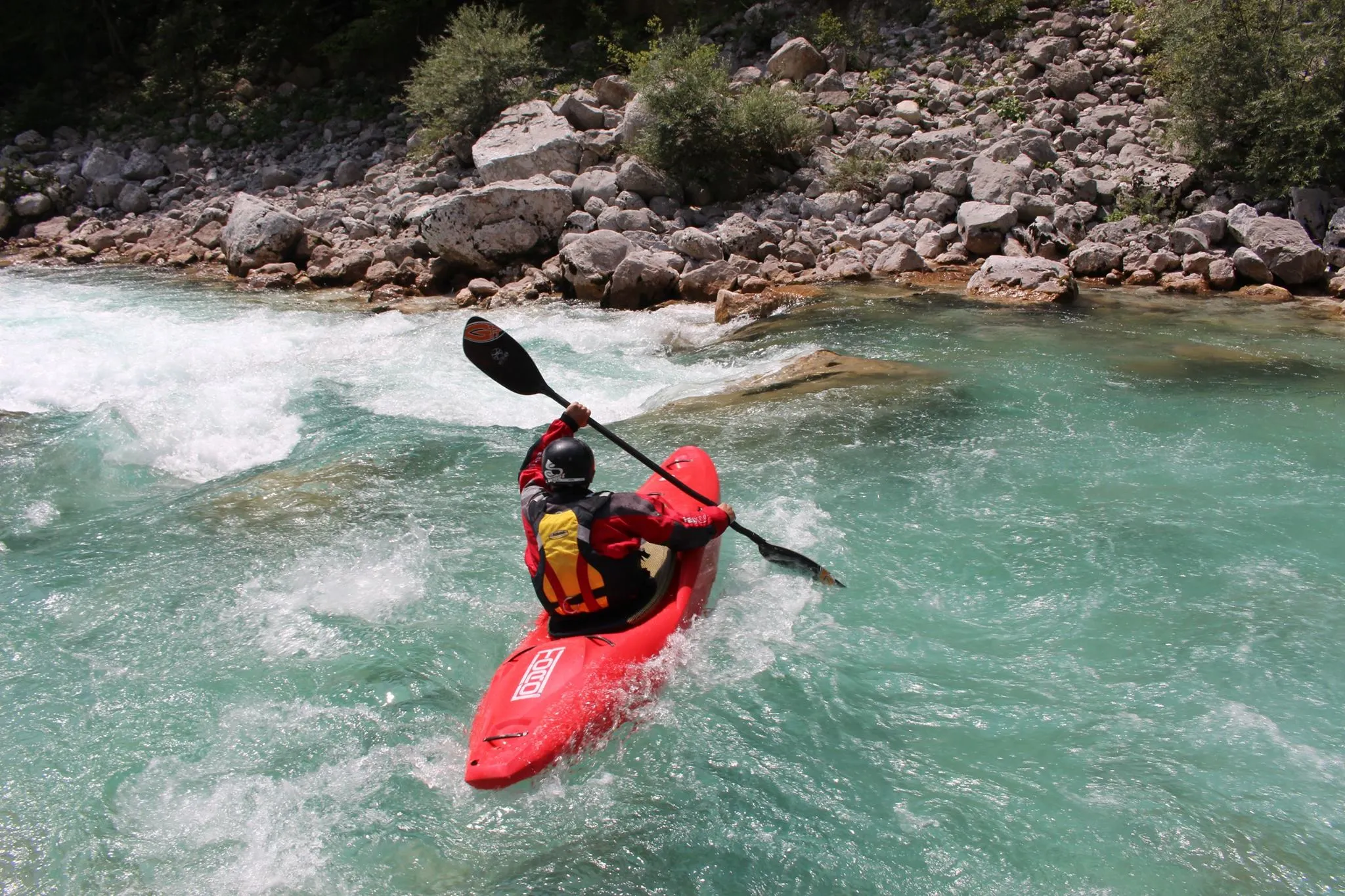 a kayaker kining up above a rapid viewed from behind