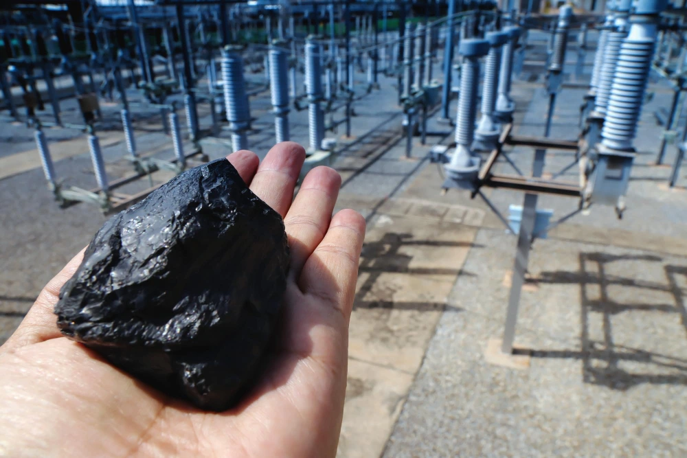 Person holding a piece of coal in his hand with electric plant the background