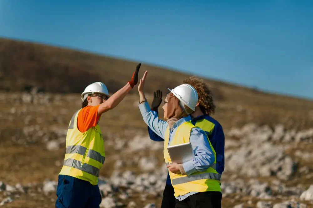 Three colleagues dressed in safety gear high five each other while in the field