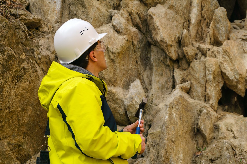 Geoscientist equipped with hard hat looking up a mountain wall