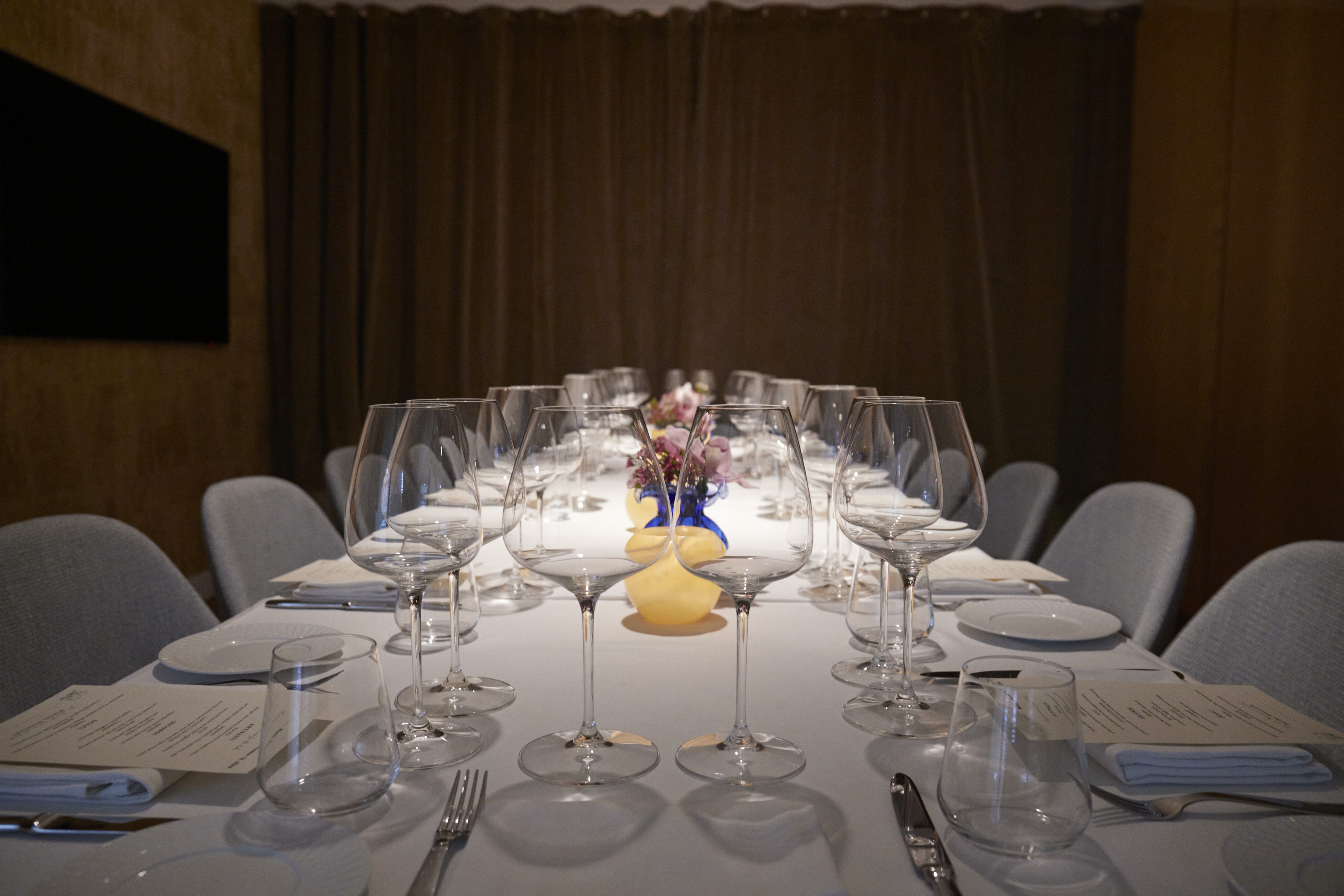 the private dining room at marea beverly hills - a long table receeding away from the viewer, covered with a white tablecloth and fully set with wine glasses, water glasses, share plates, and a specialized menu at each place setting