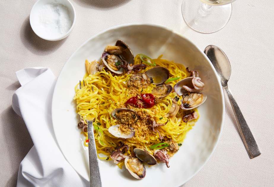 Tagliolini pasta with clams, baby squid, cherry tomatoes, and toasted breadcrumbs served in a white bowl—an elegant seafood pasta dish from Marea.