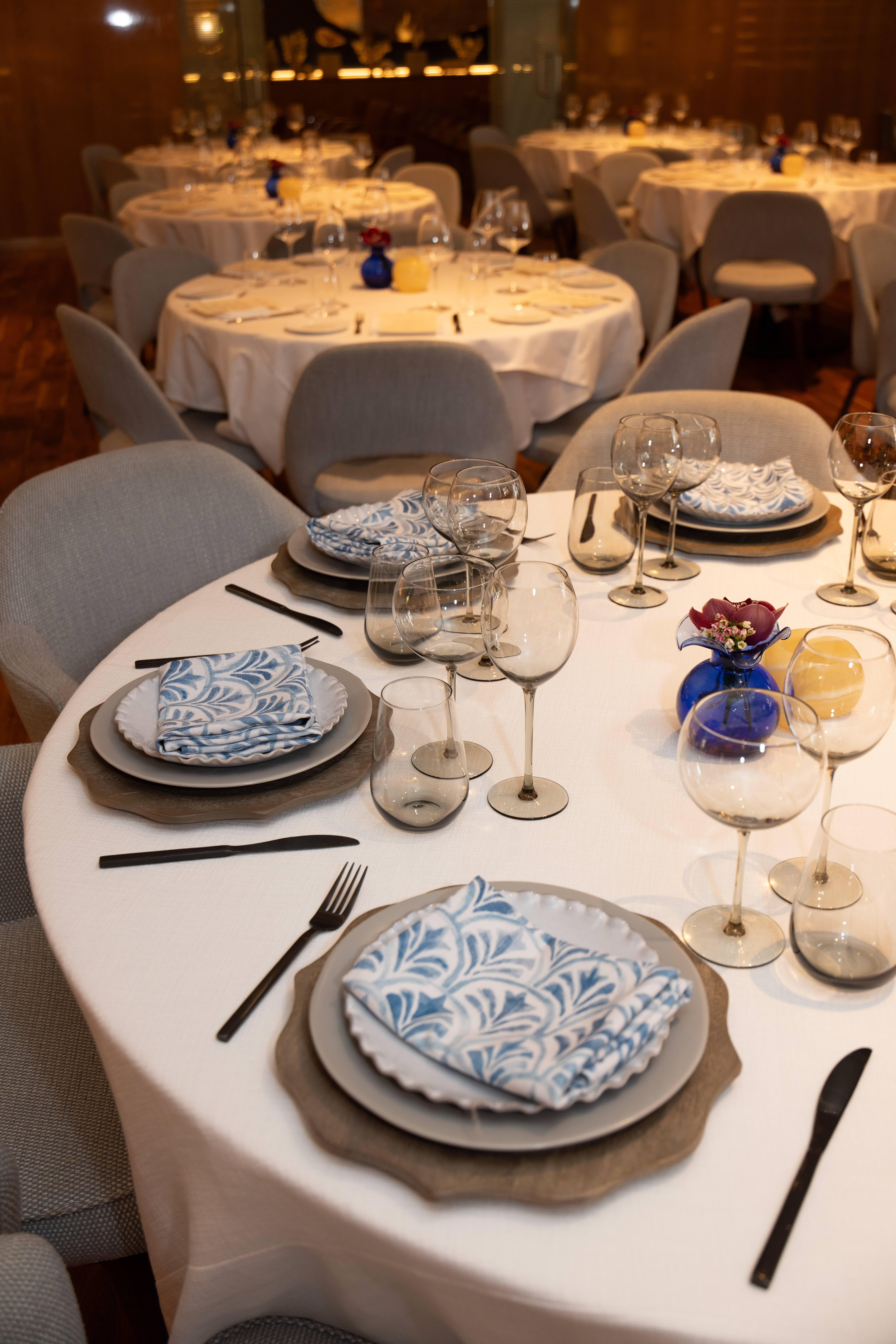 marea beverly hill's main dining room - warm wooden walls, tables with white tablecloths are fully set with white dishes and napkins, along with blue glass bud vases