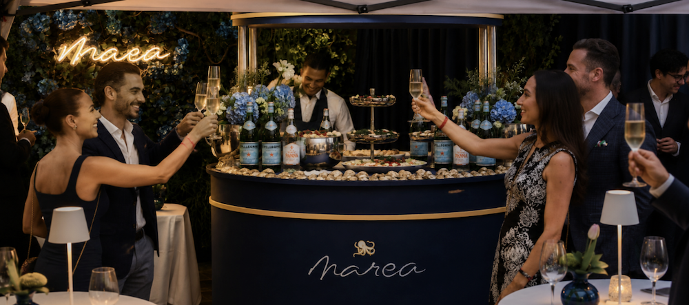 people holding up wine glasses in front of a Marea wine cart