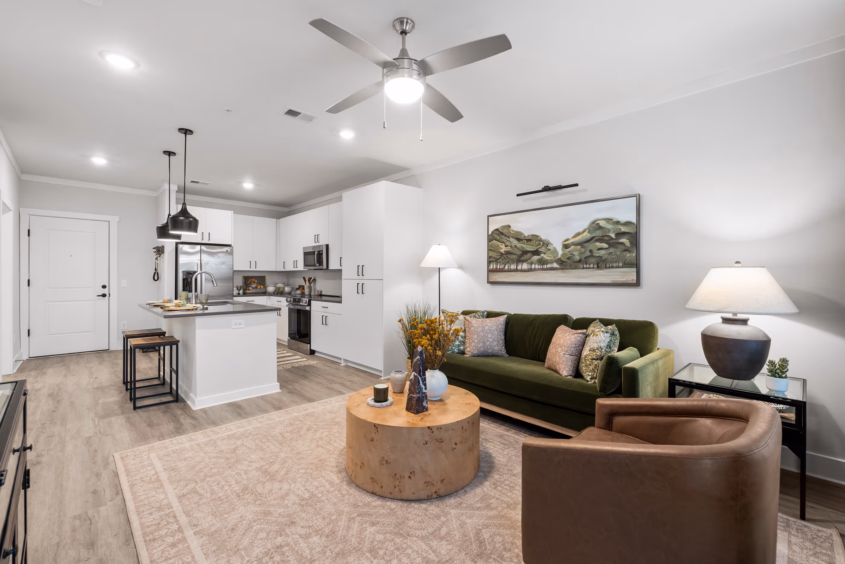 Modern open-concept living room and kitchen in an apartment at The Abbey in Greenville, SC, featuring a green sofa, white kitchen island, and contemporary decor.
