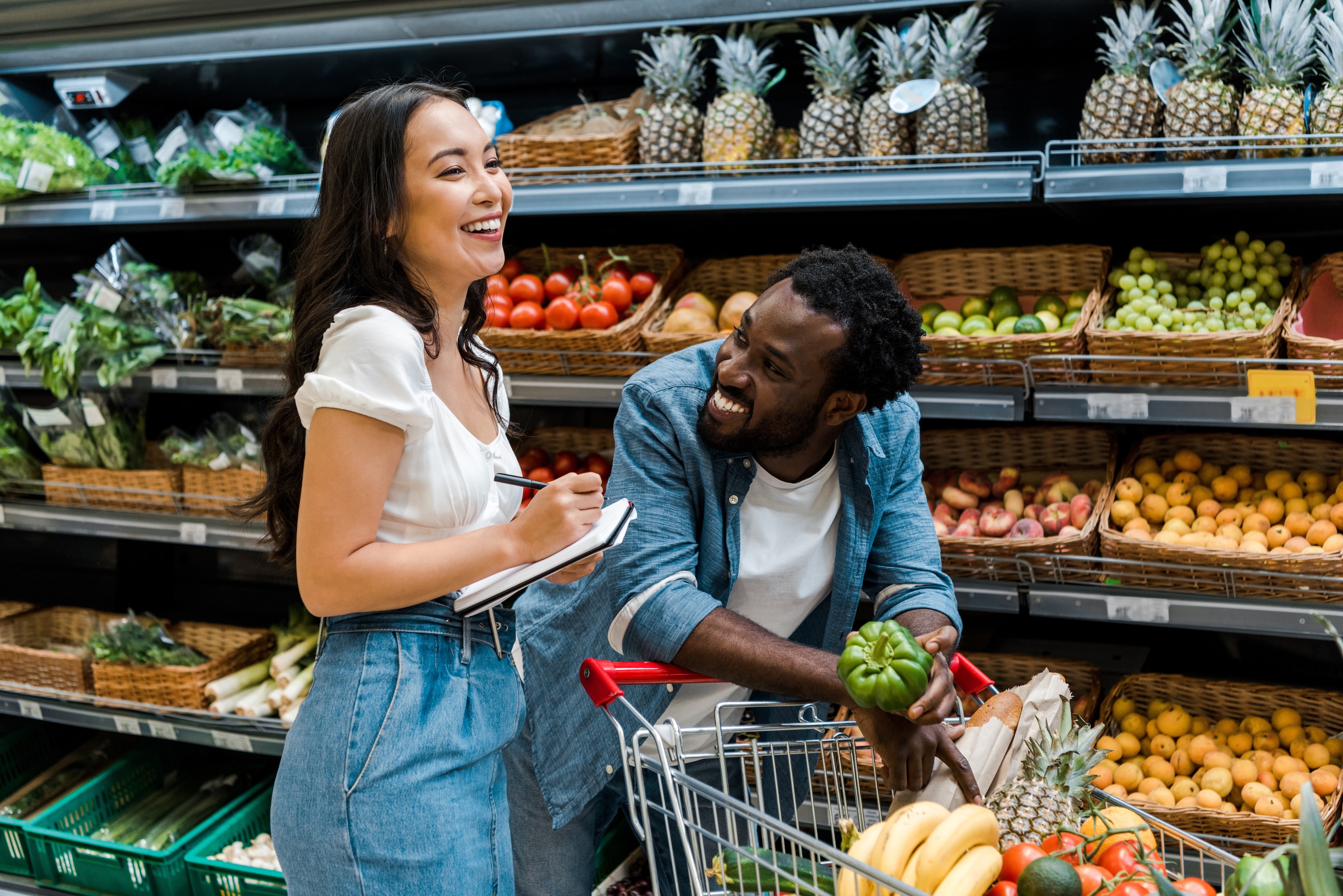 A happy couple smiling while grocery shopping for fresh produce, representing the convenience of local amenities near The Abbey in Greenville, SC.