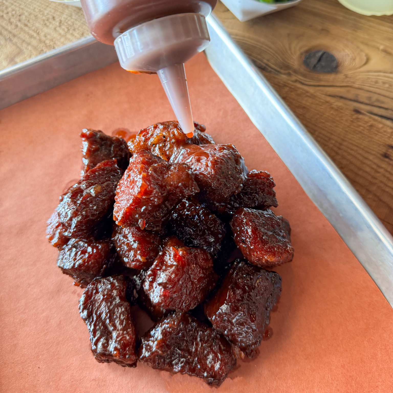 Someone pouring barbecue sauce on a pile of "Burnt Ends" brisket.