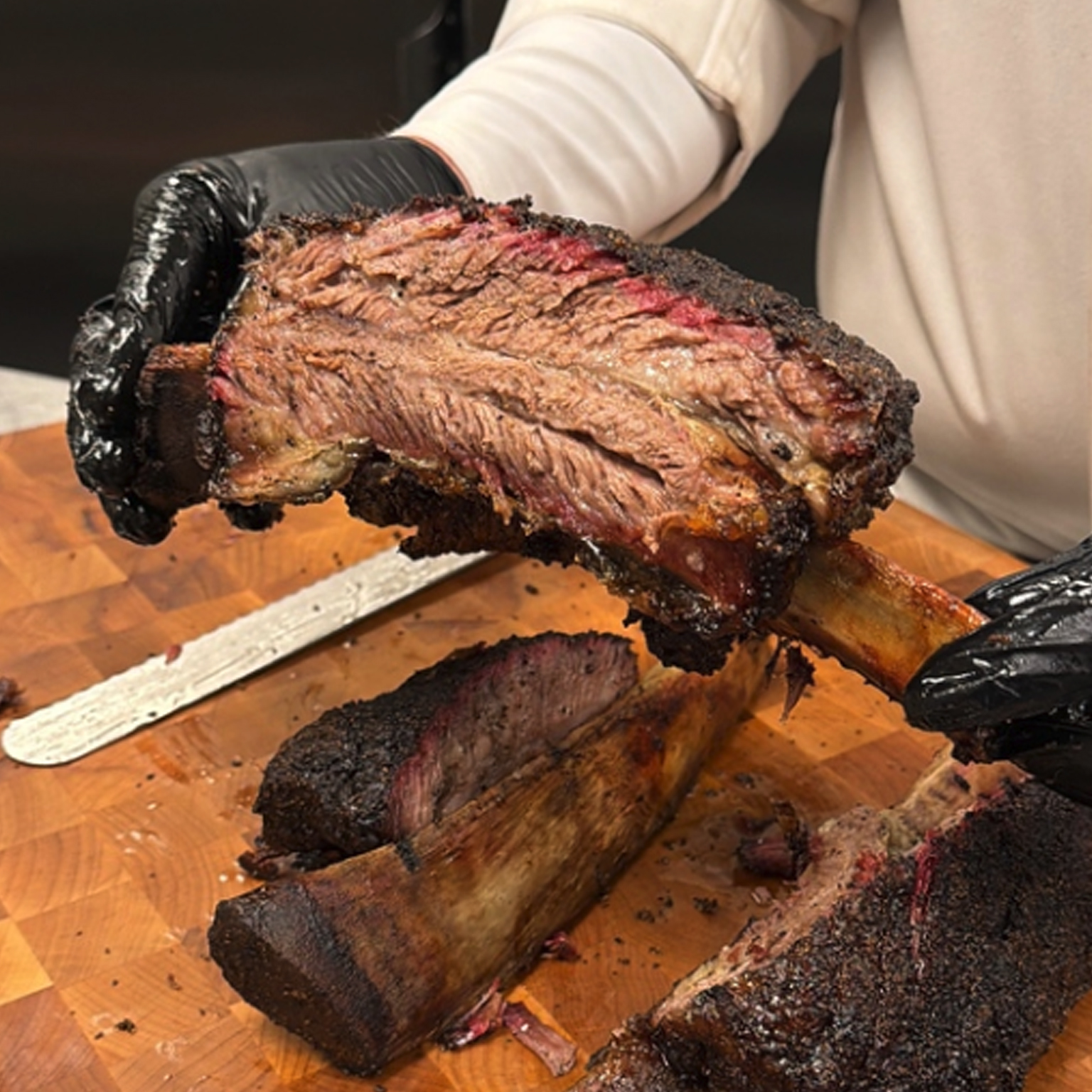 A chef holding a piece of Dino rib above a rack of beef ribs.
