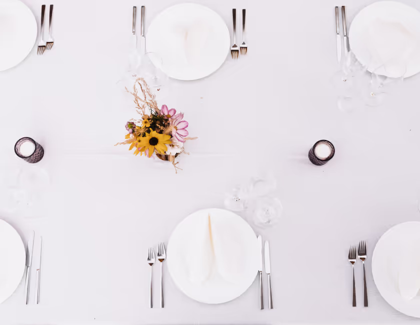Smaakvol gedekte tafel met wit tafelkleed, servies, bestek, glazen en bloemen in het midden.