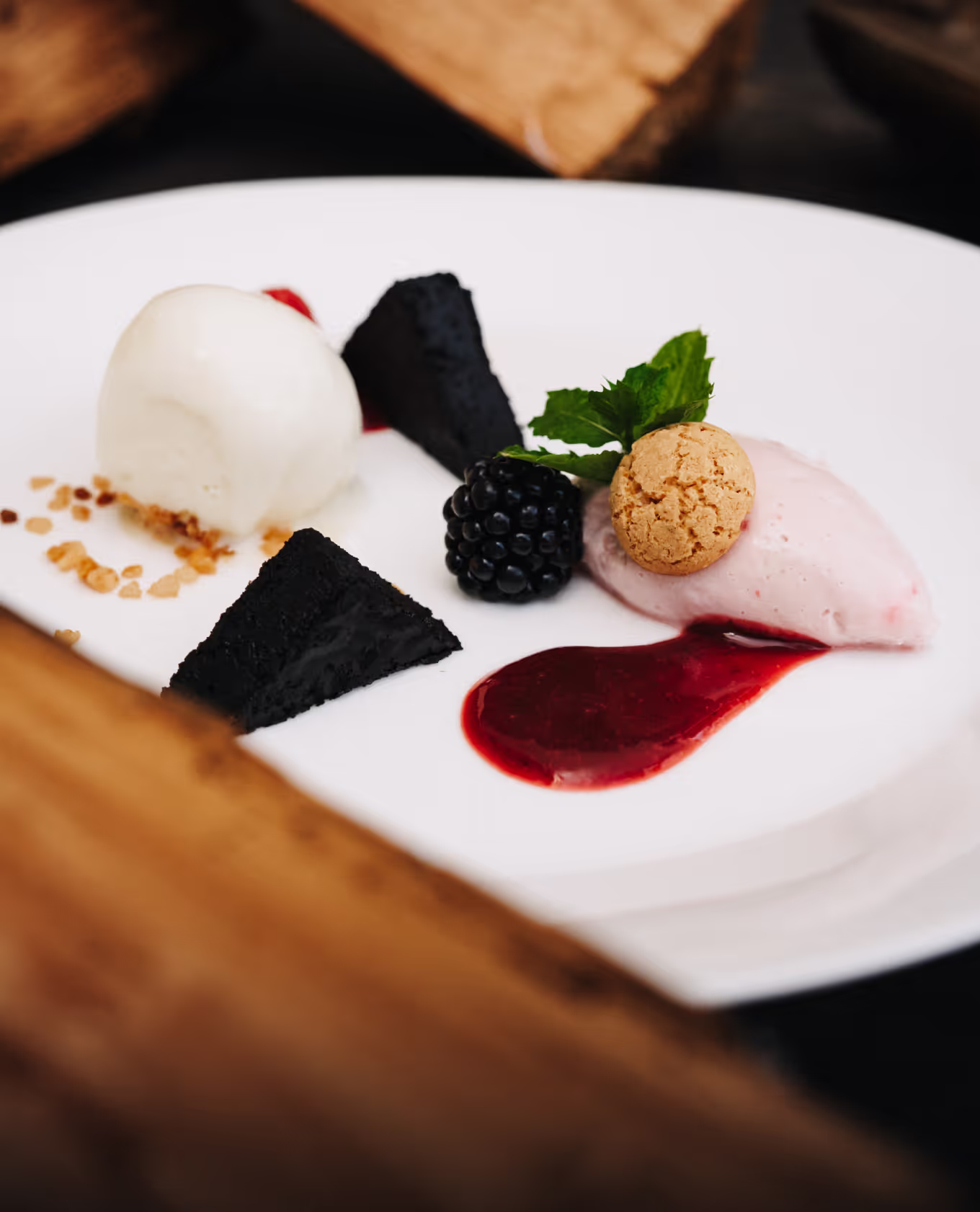 Gastrisch dessert met braambes, twee stukjes zwarte cake, roomijs, slagroom, een krokant koekje en rode vruchtensaus.