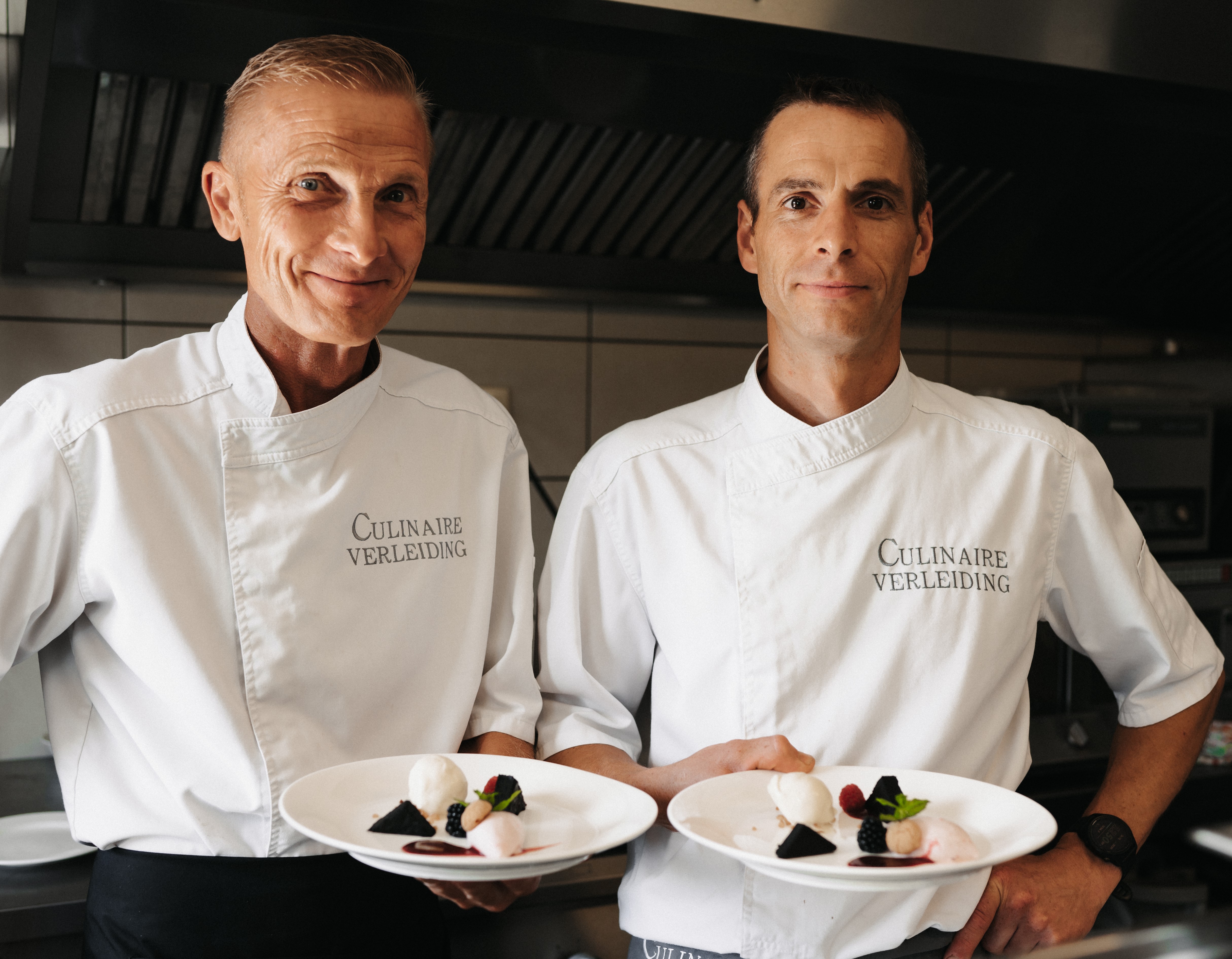 Twee koks in witte jassen die desserts op witte borden presenteren in een keuken.
