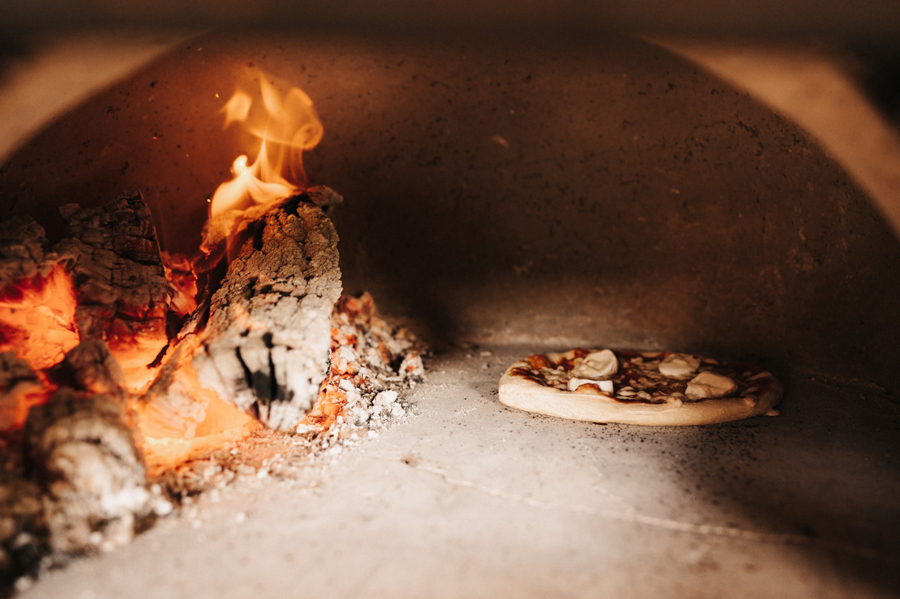 Pizza bakt in een traditionele houtoven met brandend hout aan de linkerkant.