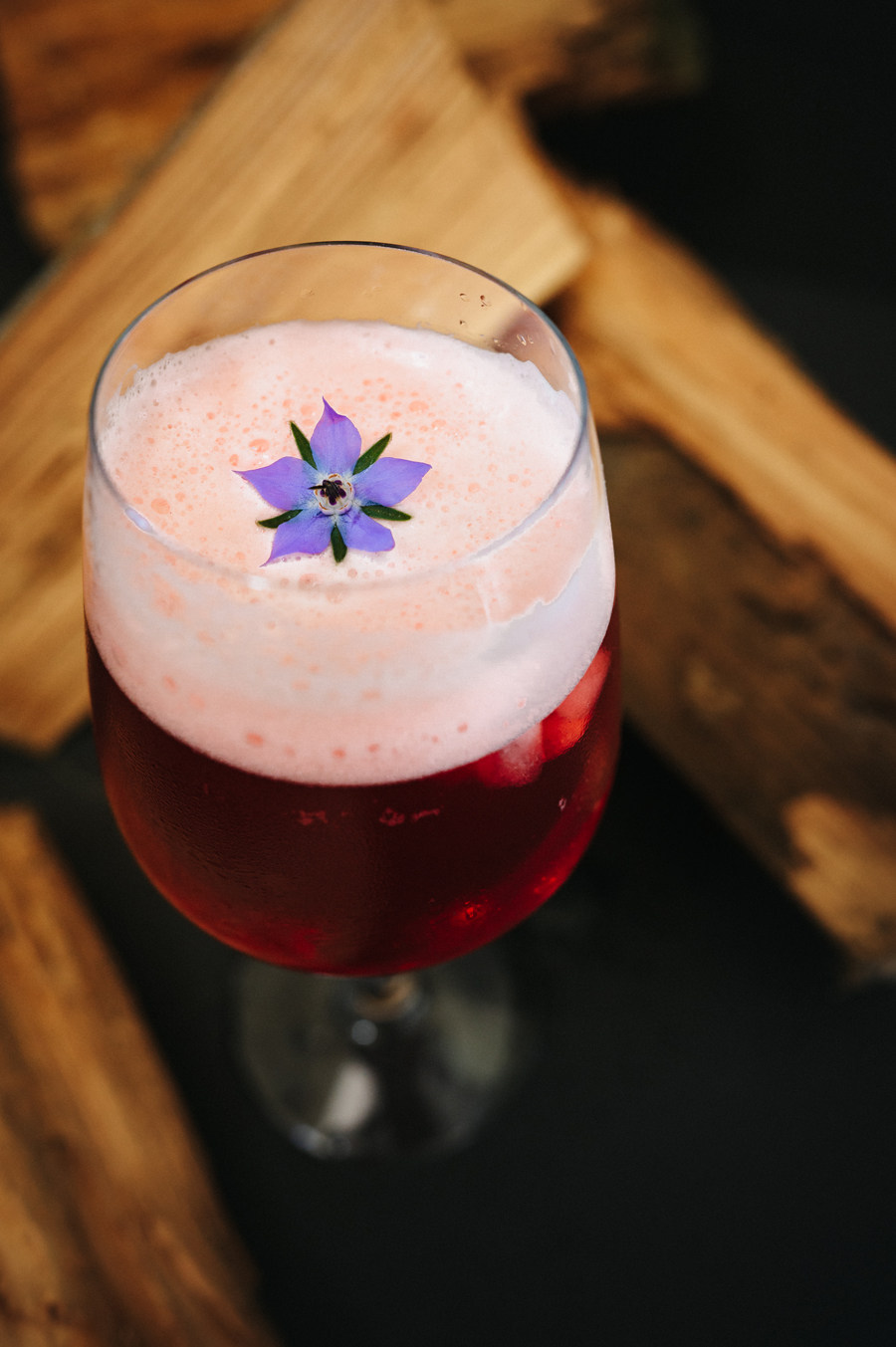 Glas met rood drankje met schuim en een paars bloemetje als garnering.