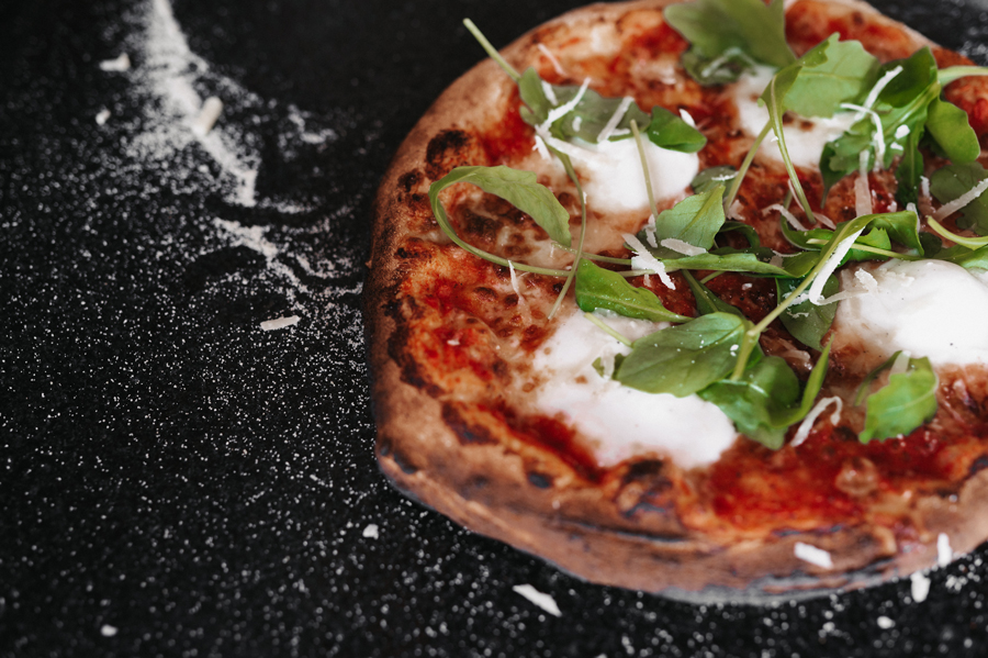 Pizza met kaas, tomatensaus en verse groene bladeren op zwarte achtergrond met bloem.