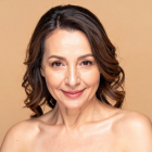 Smiling middle-aged woman with skin aging against a beige background.