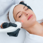 Woman receiving a non-invasive facial treatment with a handheld device by a professional wearing black gloves.