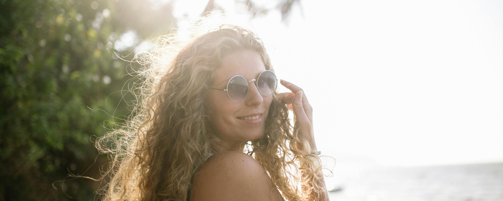 Close-up of a woman with clear, glowing skin and natural makeup, smiling softly against a light background.
