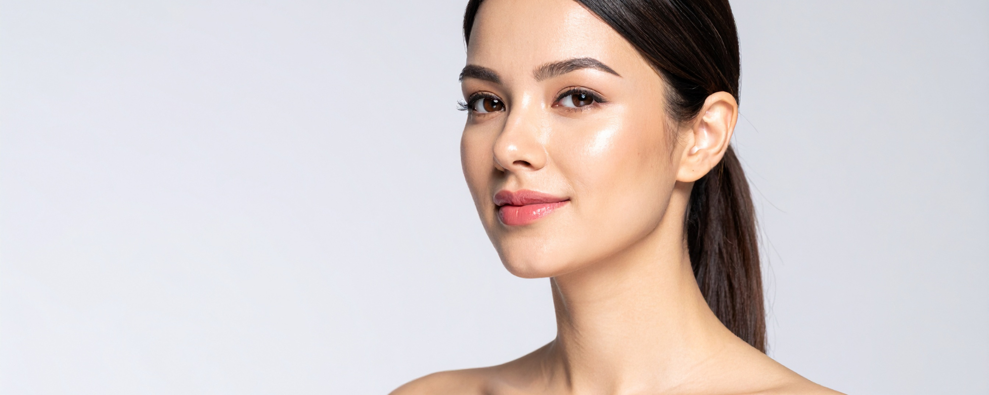 Close-up of a woman with clear, glowing skin and natural makeup, smiling softly against a light background.