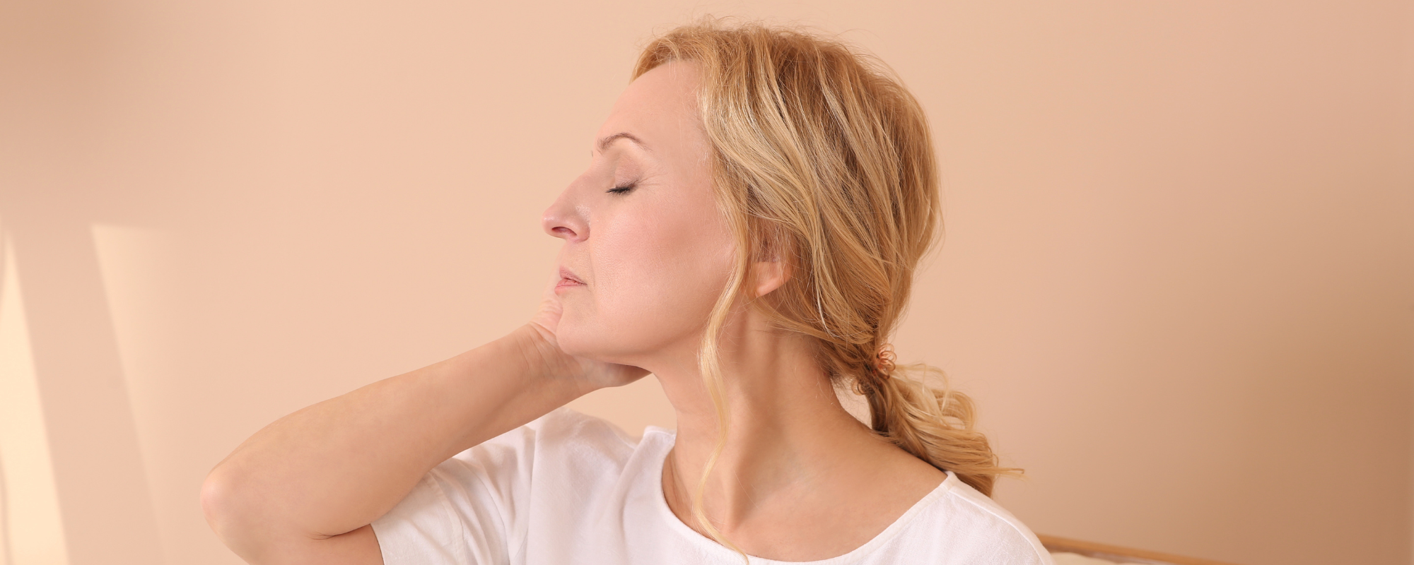Side profile of a smiling woman with clear, glowing skin and dark hair against a light taupe background.