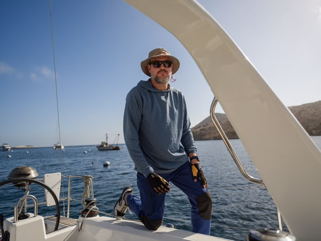 Photo of Jim DeCorpo on a sailboat with ocean and hills in the background.