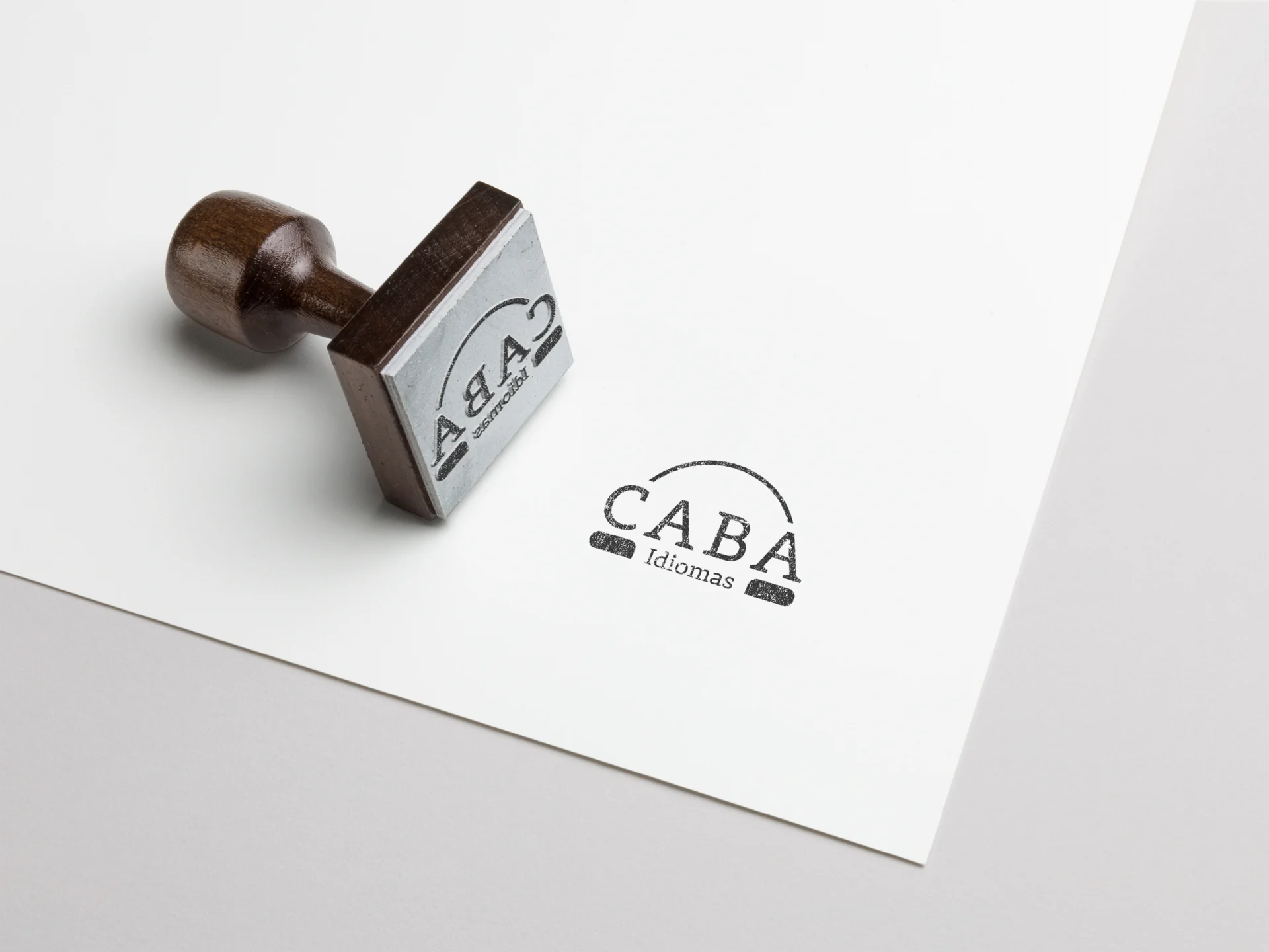 Carimbo de madeira e aplicação monocromática da marca CABA Idiomas sobre papel.