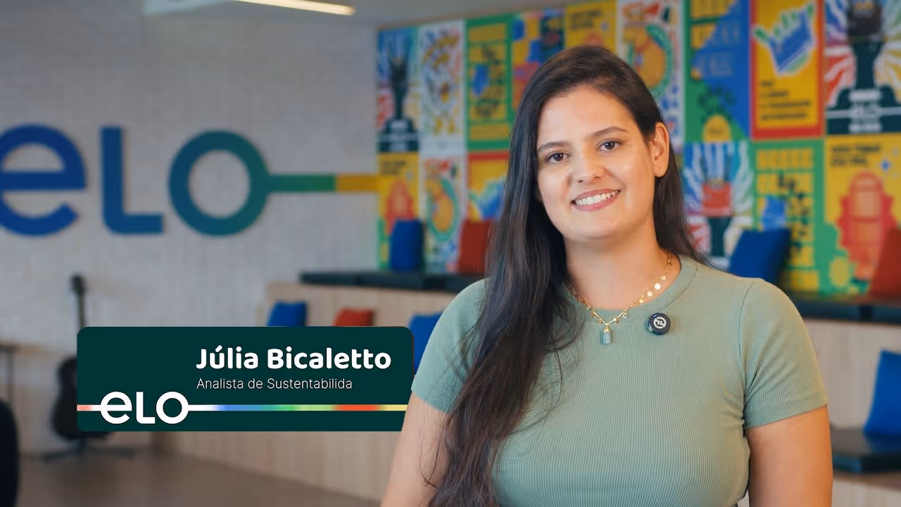 Júlia Bicaletto sorri, analista de sustentabilidade em ambiente colorido de escritório Elo.