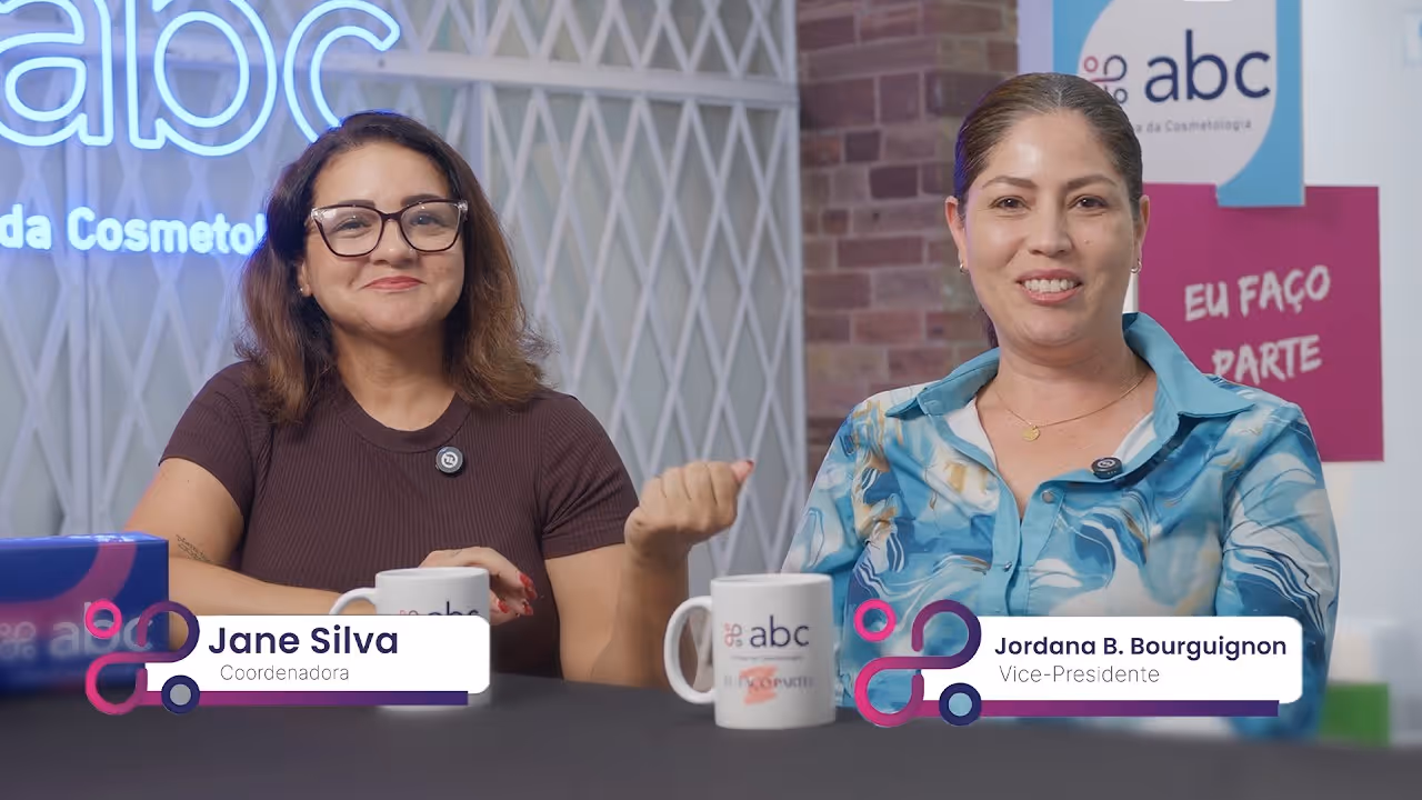 Jane Silva e Jordana B. Bourguignon, da associação brasileira de cosmetologia, sentadas em mesa com canecas, sorrindo para a câmera.