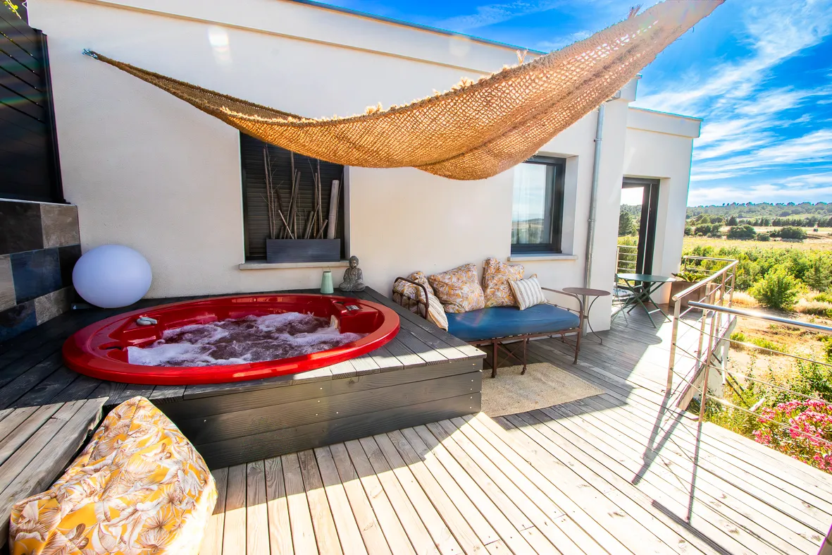 Vue extérieure du gîte avec jacuzzi privatif, idéal pour un moment de relaxation en couple.