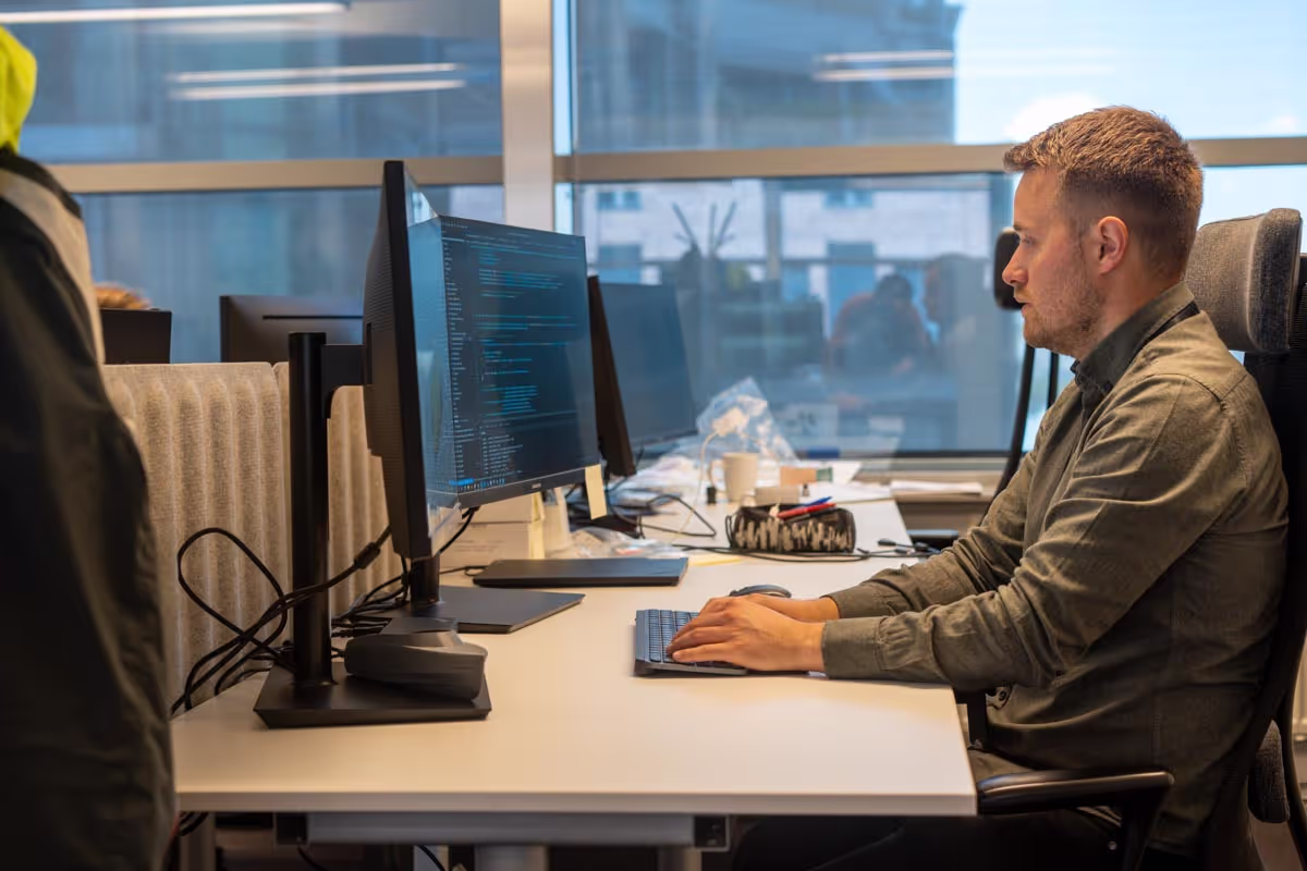 Man sitting at an office desk working on a computer with code displayed on the monitor.