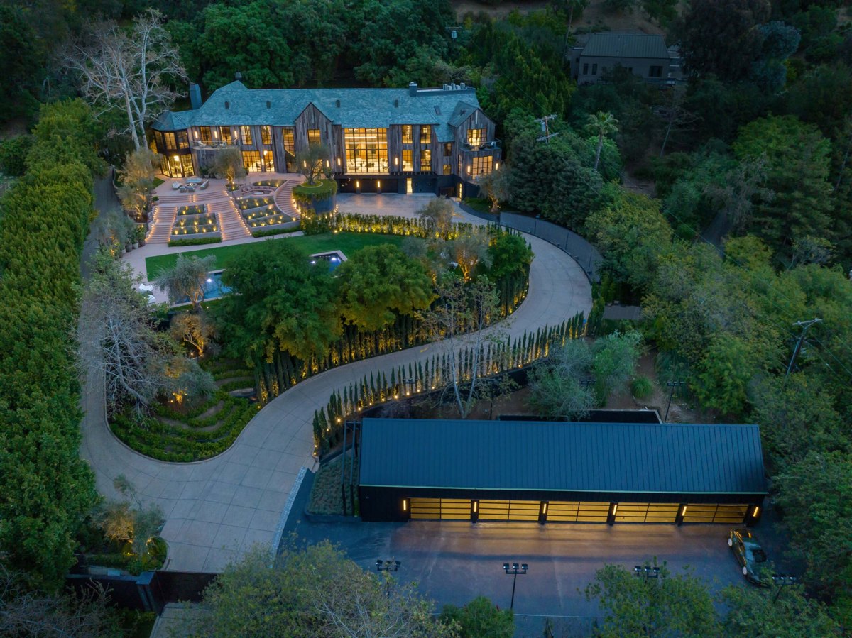 Aerial view at dusk of a Benedict Canyon estate set into the canyon, with terraced grounds and a lit driveway winding down the hill